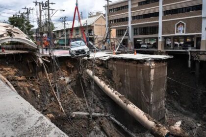 At a central junction, in front of a local police station and Vajira Hospital in a residential district of Bangkok, a roughly 50-metre (160-foot) hole pulled down power lines and revealed a burst pipe gushing water. Dozens of police and city officials blocked off the site to prevent more damage and fatalities, when this happened a pickup truck teetered precariously on the edge of the hole. Suriyachai Rawiwan, director of Bangkok’s disaster prevention department, present at the scene reported that the collapse was likely linked to recent heavy rain and a leaky pipe.